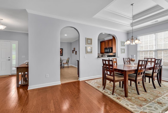 dining space featuring crown molding, arched walkways, and light wood-type flooring