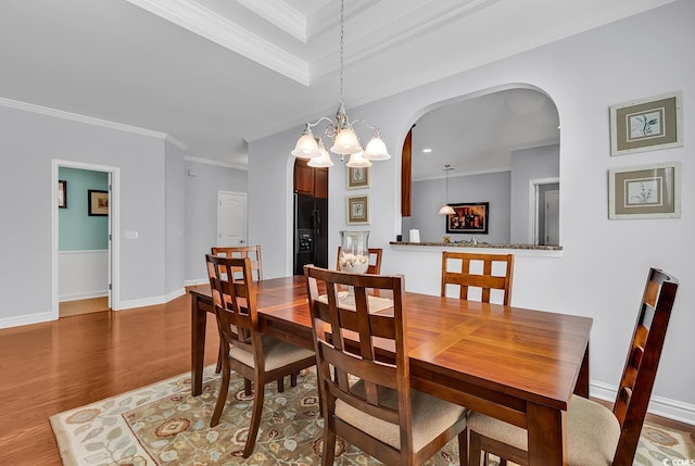 dining room with crown molding, arched walkways, wood finished floors, baseboards, and a chandelier