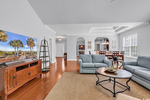 living area featuring ornamental molding, wood finished floors, baseboards, a tray ceiling, and arched walkways