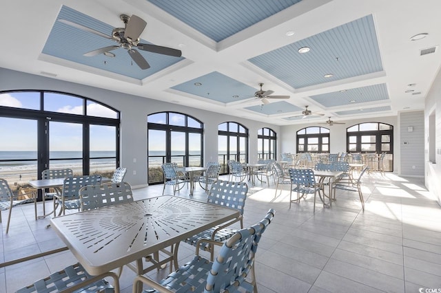 interior space with a ceiling fan, light tile patterned floors, a water view, visible vents, and coffered ceiling