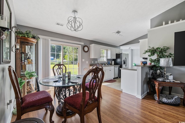 dining area featuring light wood-style floors, lofted ceiling, and a textured ceiling