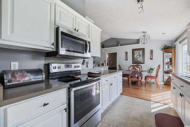 kitchen featuring stainless steel appliances, vaulted ceiling, white cabinets, and a textured ceiling