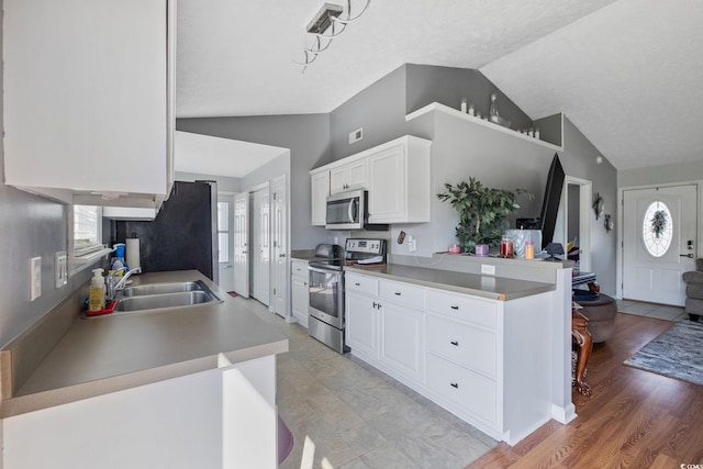 kitchen with stainless steel appliances, lofted ceiling, a sink, white cabinetry, and a textured ceiling