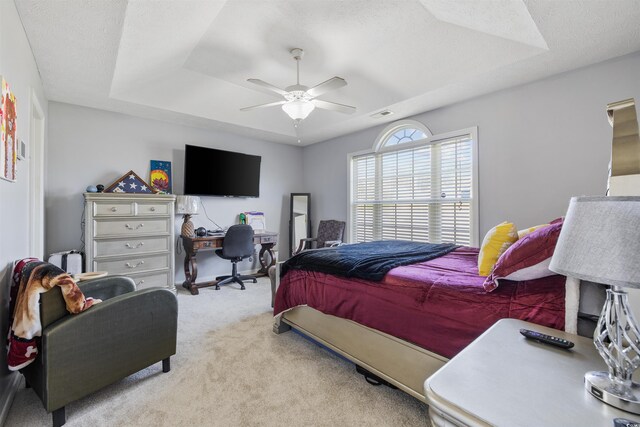 carpeted bedroom featuring a raised ceiling, a desk, and a ceiling fan