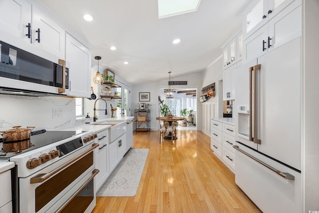 kitchen with a sink, white appliances, light countertops, and white cabinets