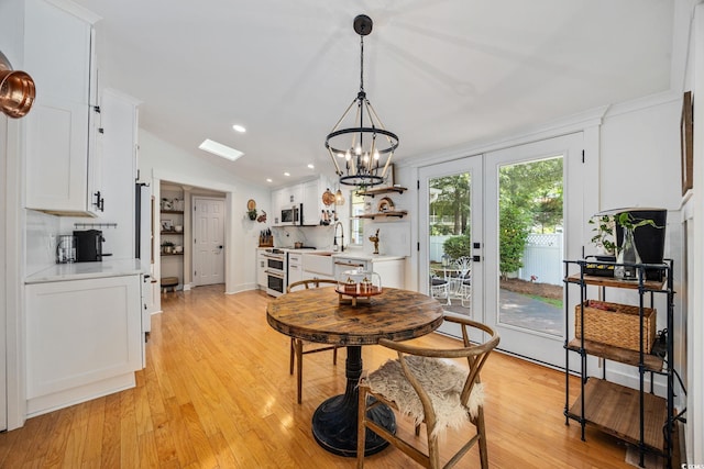 dining area with vaulted ceiling, light wood-style flooring, and a notable chandelier