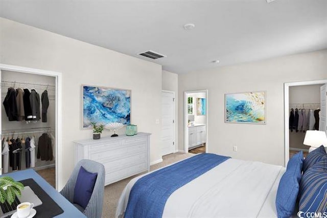 bedroom with a closet, visible vents, light colored carpet, connected bathroom, and a spacious closet