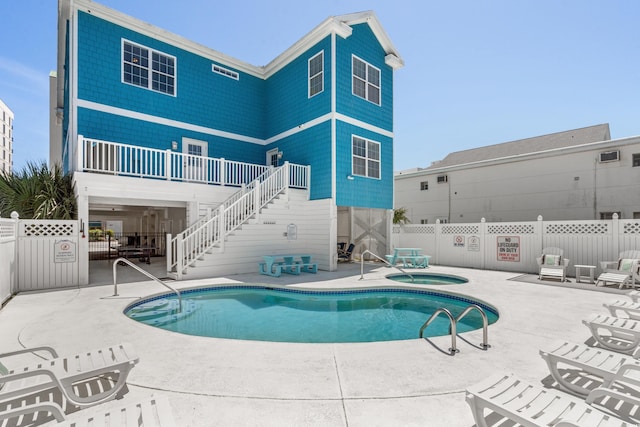 back of property with fence, a community pool, a patio area, a hot tub, and stairway