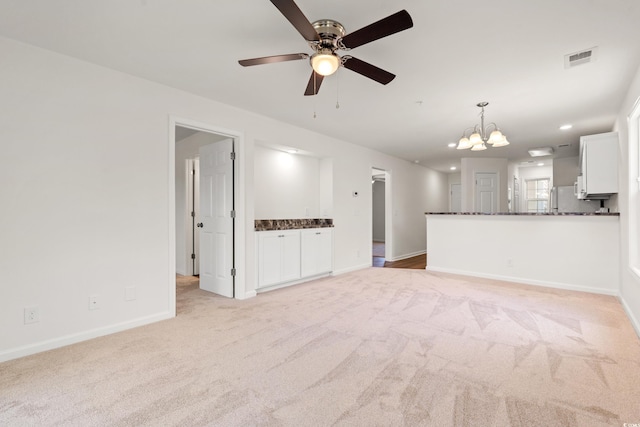 unfurnished living room featuring light carpet, ceiling fan with notable chandelier, recessed lighting, baseboards, and visible vents