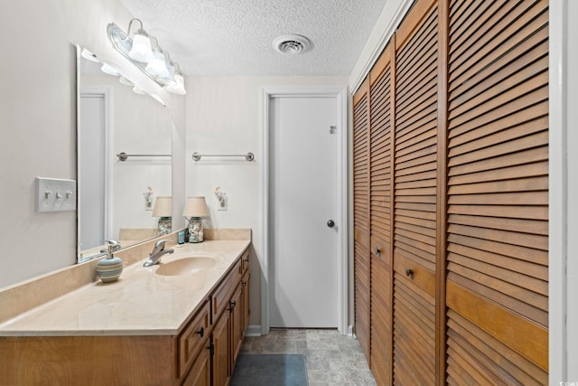 bathroom with vanity, a textured ceiling, visible vents, and a closet