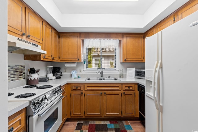 kitchen with brown cabinets, a sink, white appliances, light countertops, and under cabinet range hood