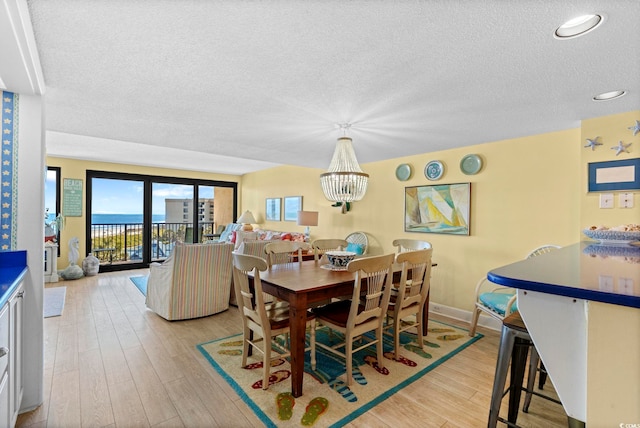 dining room with a textured ceiling, baseboards, a notable chandelier, light wood-style floors, and recessed lighting