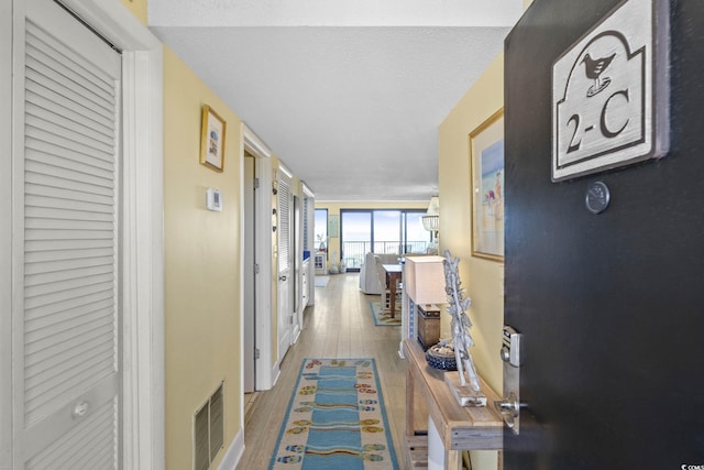 hall featuring baseboards, wood finished floors, and visible vents