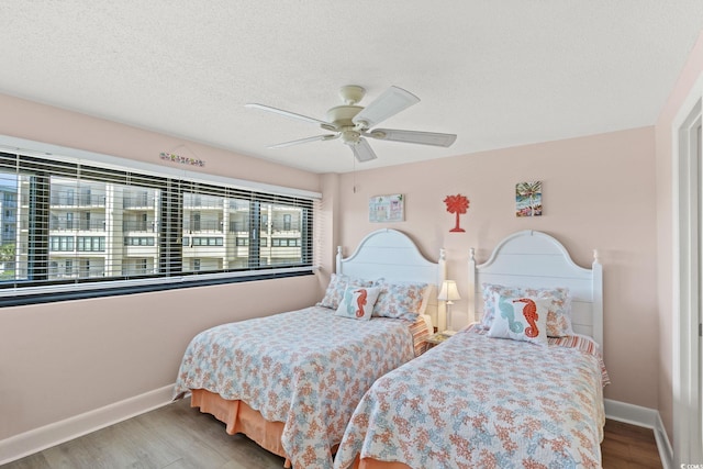 bedroom featuring baseboards, a textured ceiling, ceiling fan, and wood finished floors
