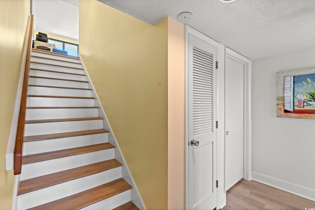 stairway with a textured ceiling, baseboards, and wood finished floors