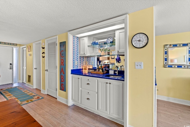 bar with a sink, a textured ceiling, indoor wet bar, baseboards, and light wood-type flooring