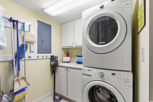 laundry area featuring electric panel, a textured ceiling, cabinet space, stacked washing maching and dryer, and baseboards