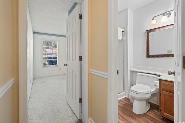 full bath with a stall shower, a textured ceiling, toilet, vanity, and wood finished floors