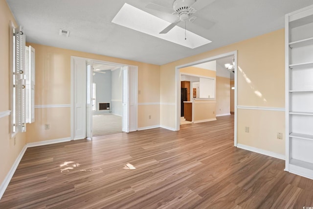 spare room featuring a ceiling fan, light wood-style floors, a skylight, and baseboards
