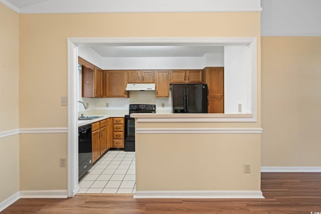 kitchen with under cabinet range hood, light wood finished floors, a sink, black appliances, and light countertops