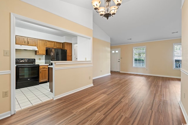kitchen with brown cabinetry, a notable chandelier, black appliances, under cabinet range hood, and light wood-style floors
