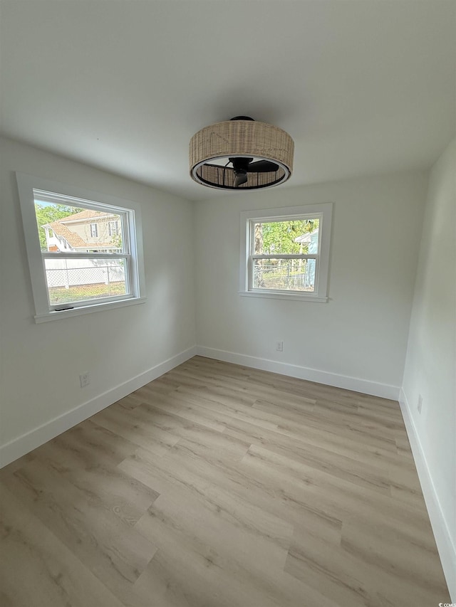 spare room with baseboards, a wealth of natural light, and light wood-style floors