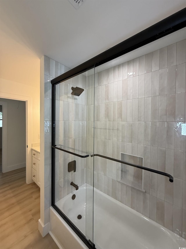 bathroom featuring baseboards, enclosed tub / shower combo, wood finished floors, and vanity