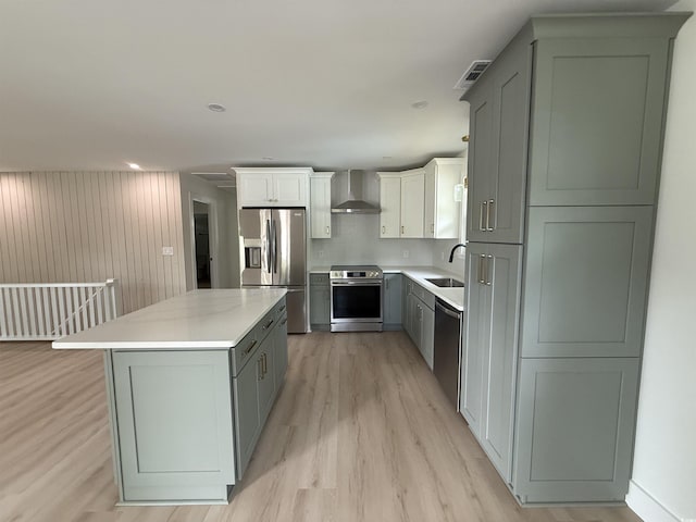 kitchen featuring wall chimney range hood, appliances with stainless steel finishes, light wood-type flooring, a sink, and light countertops