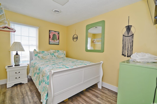 bedroom with a textured ceiling, baseboards, visible vents, and wood finished floors