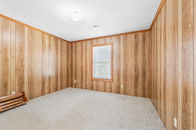 carpeted spare room featuring wooden walls, visible vents, and a textured ceiling