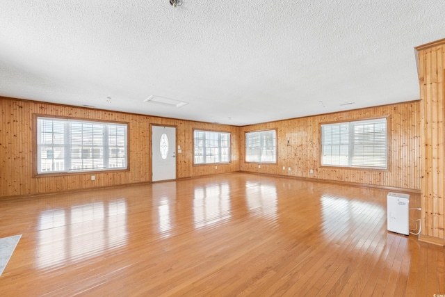 unfurnished living room featuring wood walls, light wood-style flooring, and a textured ceiling