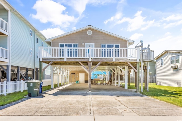 beach home featuring concrete driveway, fence, a wooden deck, and a carport