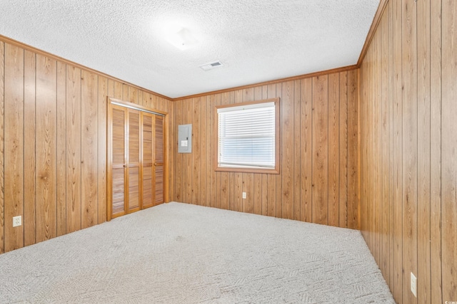 carpeted empty room with electric panel, wooden walls, a textured ceiling, and visible vents