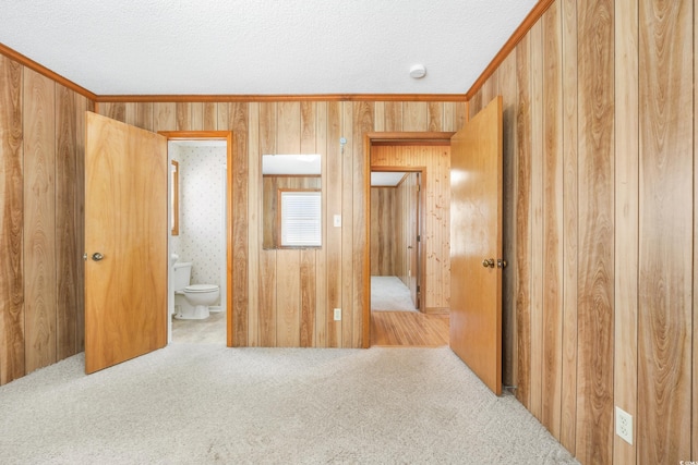 unfurnished bedroom featuring a textured ceiling, ensuite bath, wood walls, and carpet floors