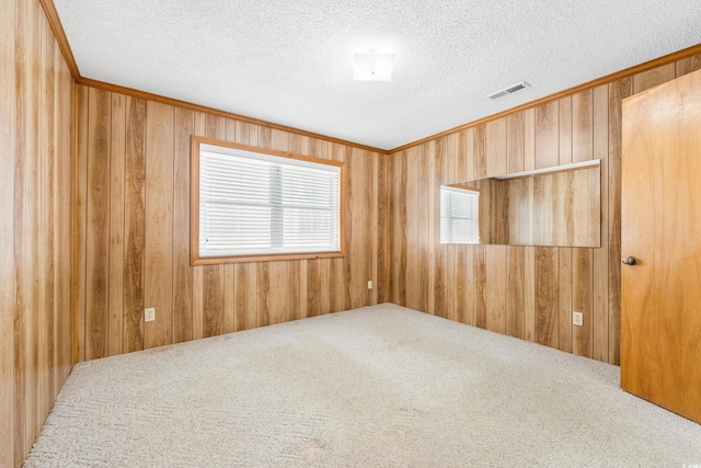 carpeted empty room with wood walls, a textured ceiling, and visible vents