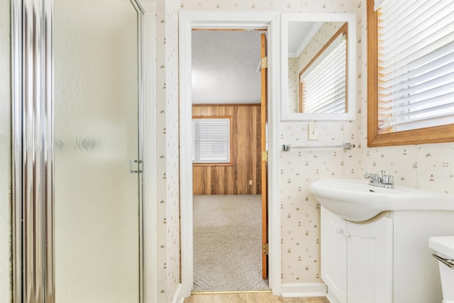 full bath with a shower stall, wooden walls, vanity, and wallpapered walls