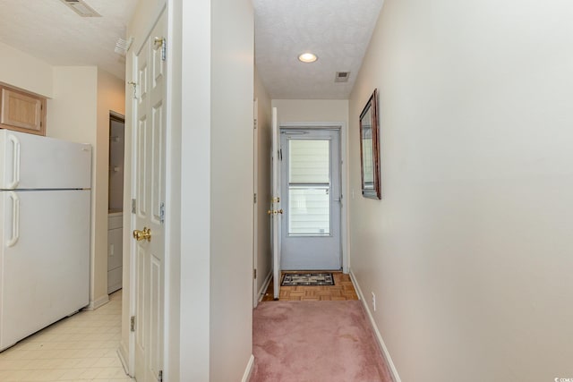 hallway with a textured ceiling, visible vents, baseboards, and washer / clothes dryer