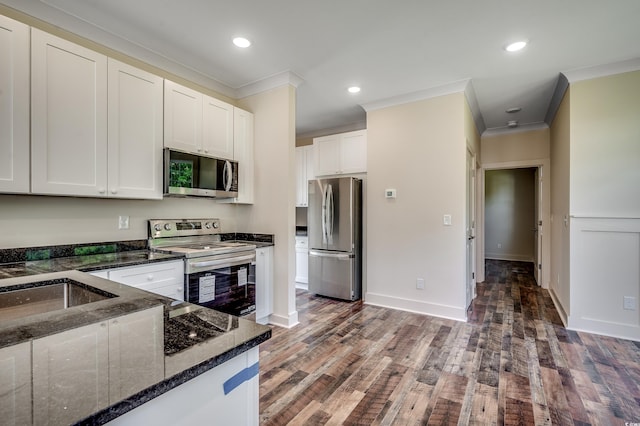 kitchen featuring dark stone countertops, wood finished floors, ornamental molding, white cabinetry, and appliances with stainless steel finishes