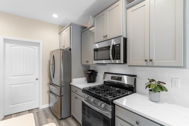 kitchen featuring light wood-style floors, gray cabinetry, decorative backsplash, and appliances with stainless steel finishes