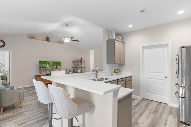 kitchen featuring a sink, a peninsula, gray cabinets, a breakfast bar, and appliances with stainless steel finishes