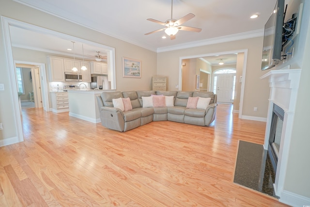 living area featuring crown molding, light wood finished floors, ceiling fan, and a fireplace with flush hearth