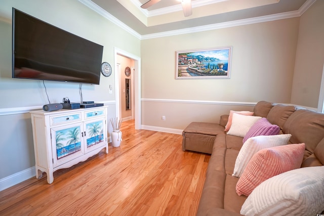 living room featuring a tray ceiling, light wood finished floors, ornamental molding, and ceiling fan