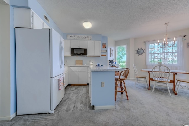kitchen featuring freestanding refrigerator, a kitchen bar, a textured ceiling, a chandelier, and white cabinets