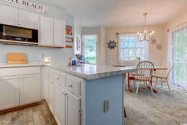 kitchen featuring a peninsula, white cabinets, a textured ceiling, a chandelier, and pendant lighting