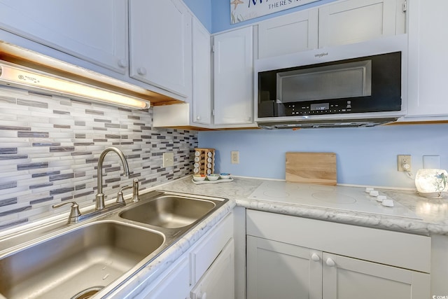 kitchen featuring stainless steel microwave, a sink, backsplash, white cabinets, and white electric stovetop
