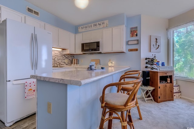 kitchen with freestanding refrigerator, stainless steel microwave, white cabinetry, light countertops, and a kitchen breakfast bar
