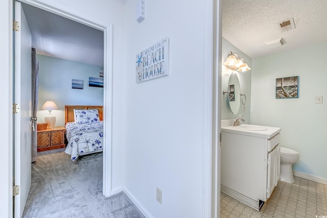 ensuite bathroom with a textured ceiling, vanity, baseboards, and toilet