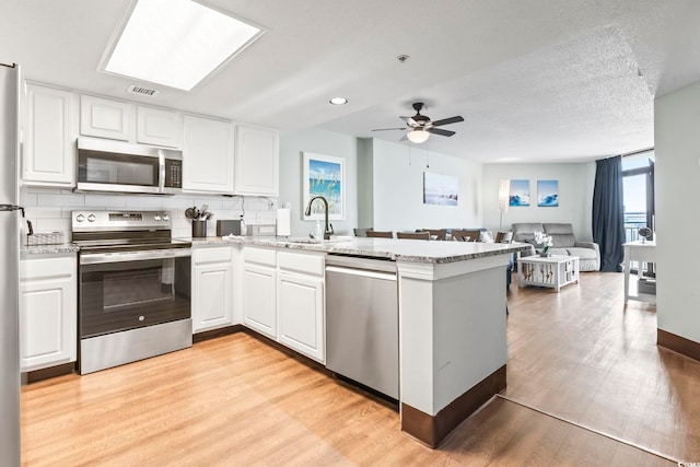 205 74th Ave N Unit 1104, Myrtle Beach, SC 29572 - kitchen with stainless steel appliances, a peninsula, a sink, light wood-type flooring, and white cabinetry