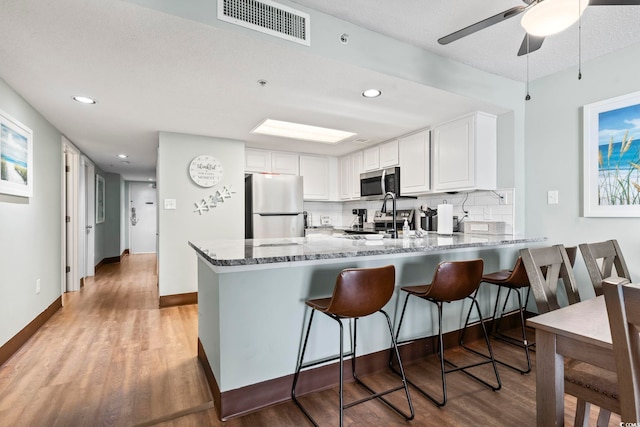 205 74th Ave N Unit 1104, Myrtle Beach, SC 29572 - kitchen featuring appliances with stainless steel finishes, a peninsula, a sink, dark stone counters, and light wood finished floors