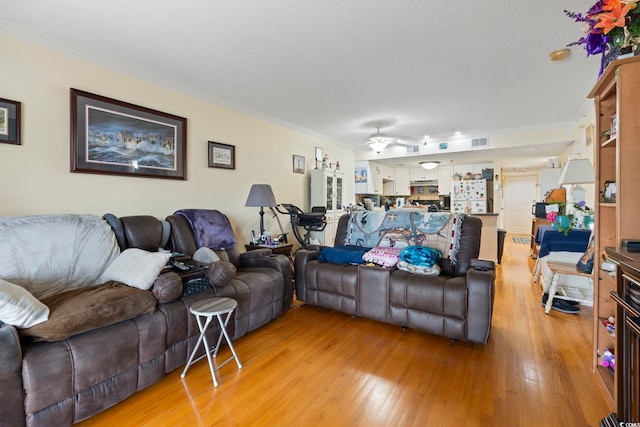 living area with a ceiling fan, crown molding, light wood-type flooring, visible vents, and a textured ceiling